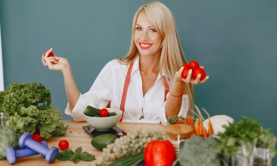 Healthy lifestyle concept with woman holding tomatoes and surrounded by fresh vegetables in a studio setting.