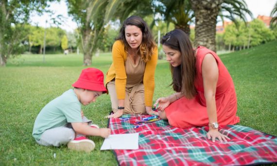 A child and two women enjoying a drawing session on a picnic blanket in a park in Portugal.
